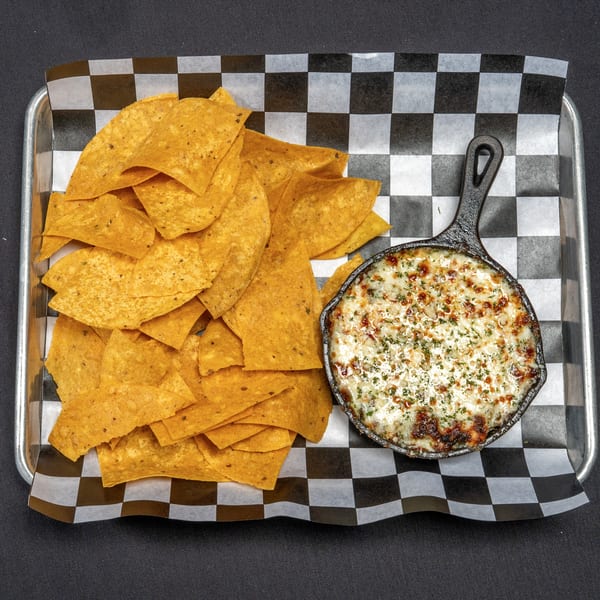 A cast iron skillet of melted cheese dip with tortilla chips on a checkered paper-lined tray.