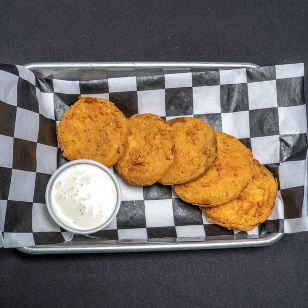 Fried green tomatoes with a side of ranch dressing in a metal tray with checkered paper.