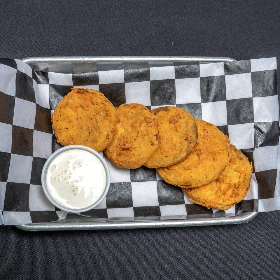 Fried green tomatoes with a side of ranch dressing in a metal tray with checkered paper.