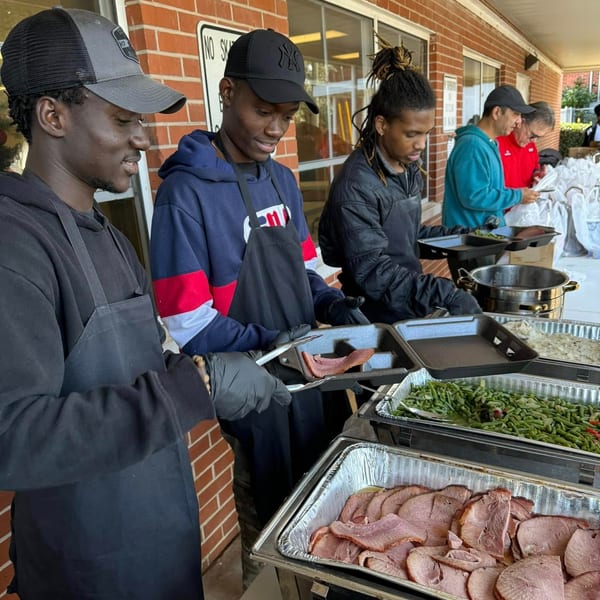 Several people serving food from chafing dishes with sliced ham, green beans, and mashed potatoes.