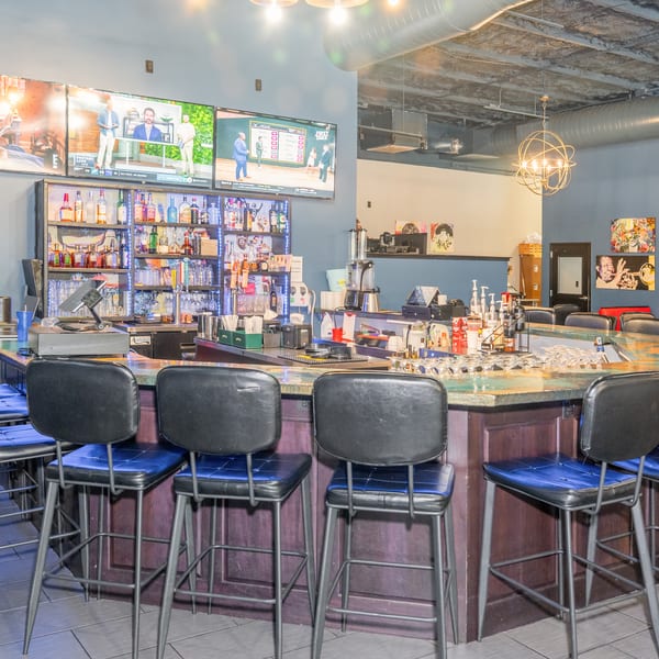 A vibrant bar area with a long, curved counter, bar stools, and multiple TVs displaying sports.
