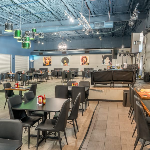 Restaurant interior with black tables and chairs, a stage, and pop art portraits on the wall.