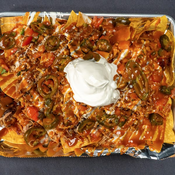 A large tray of loaded nachos with pulled pork, cheese sauce, jalapeños, and a dollop of sour cream.