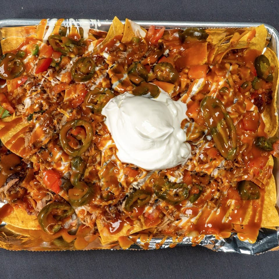 A large tray of loaded nachos with pulled pork, cheese sauce, jalapeños, and a dollop of sour cream.