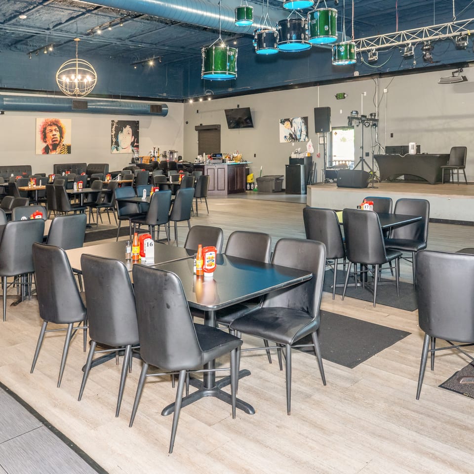 Spacious restaurant dining area with black tables and chairs, a stage, and music-themed decor.