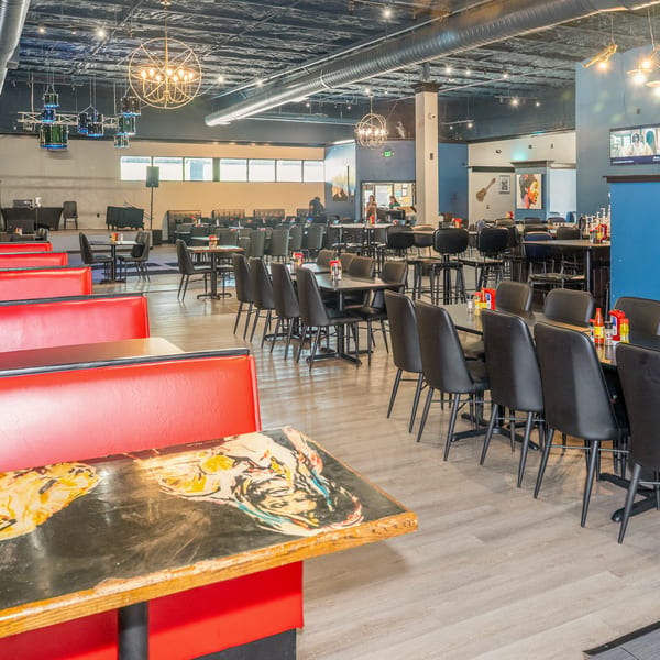Spacious restaurant interior with red booths, black tables and chairs, a stage, and modern lighting.
