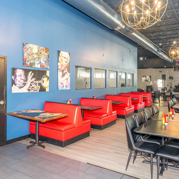 Restaurant interior with red booths, black tables and chairs, blue walls with art, and industrial ceiling.