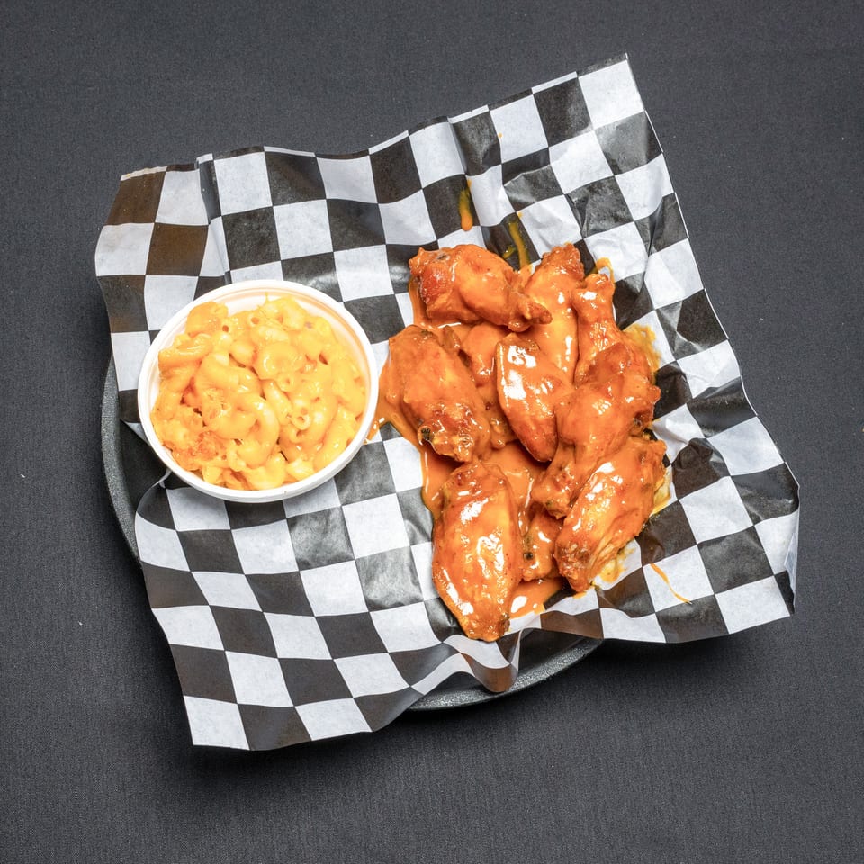 Buffalo wings and a side of macaroni and cheese on checkered paper.