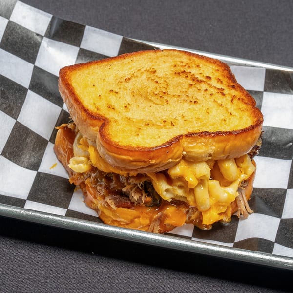 Grilled cheese sandwich filled with pulled pork, macaroni and cheese, and jalapeños on checkered paper.
