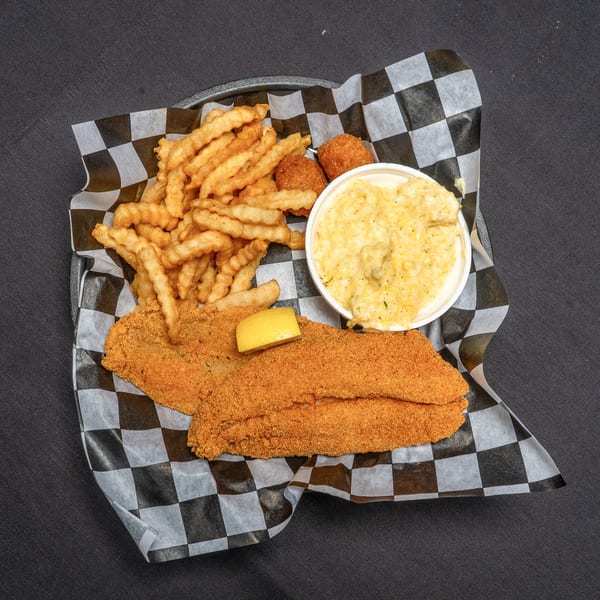Fried fish fillets with a lemon wedge, crinkle-cut fries, hush puppies, and grits on checkered paper.
