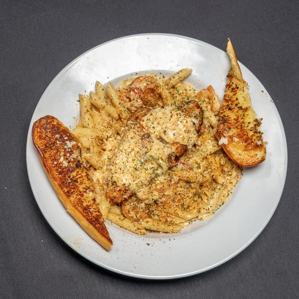 Creamy pasta with chicken, shrimp, and garlic bread on a white plate against a dark background.