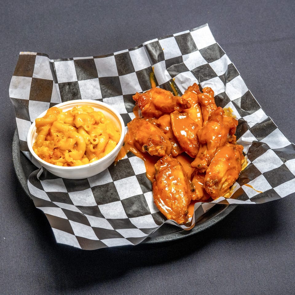A basket of buffalo wings and a side of macaroni and cheese on checkered paper.