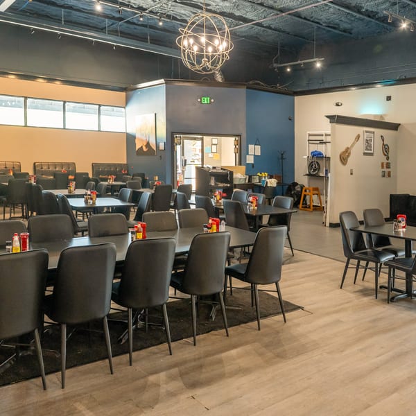 Spacious restaurant dining room with black tables and chairs, booths, and a decorative chandelier.
