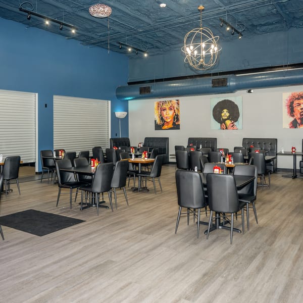 Empty restaurant dining room with black tables and chairs, blue walls, and pop art portraits.