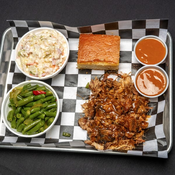 BBQ tray with pulled pork, coleslaw, green beans, cornbread, and two cups of sauce.