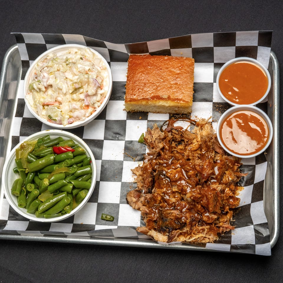 BBQ tray with pulled pork, coleslaw, green beans, cornbread, and two cups of sauce.
