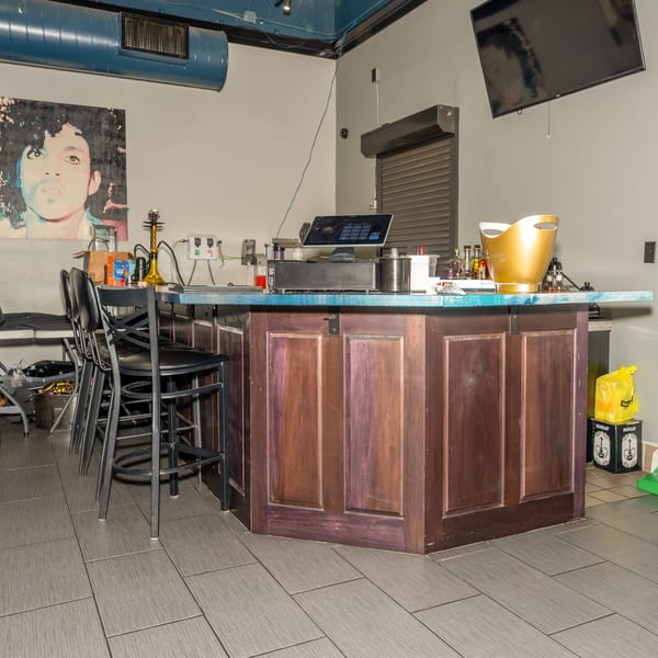 A bar area with a Prince portrait, three bar stools, and a POS system on the counter.