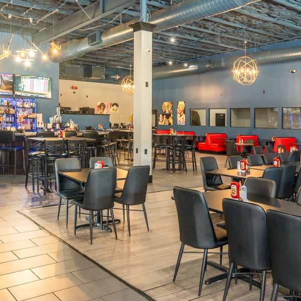 Spacious restaurant interior with a bar, high-top tables, red booths, and modern light fixtures.