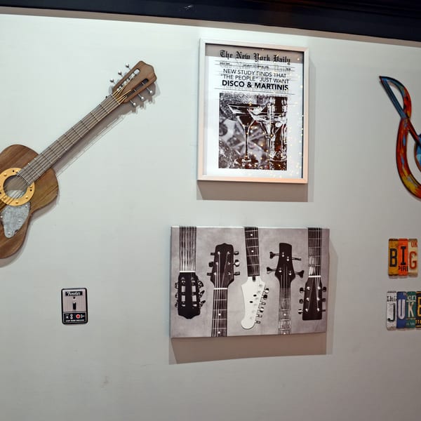Wall decor featuring a wooden guitar, framed "Disco & Martinis" print, colorful treble clef, and license plate art.