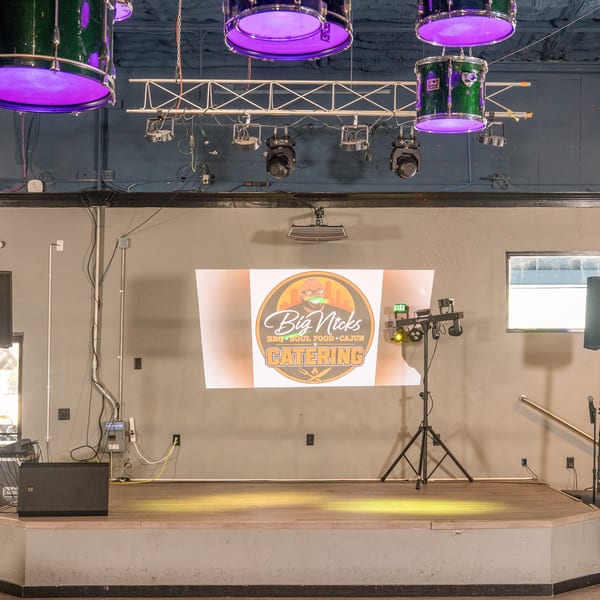An empty stage with a projector displaying the Big Nick's BBQ, Soul Food, and Cajun Catering logo.
