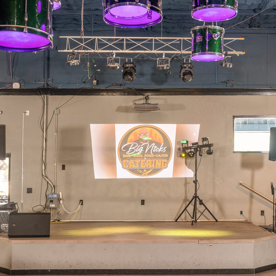 An empty stage with a projector displaying the Big Nick's BBQ, Soul Food, and Cajun Catering logo.