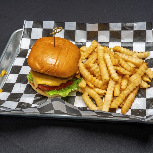 Cheeseburger with lettuce, tomato, and crinkle-cut fries on a metal tray with checkered paper.