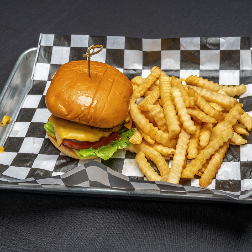 Cheeseburger with lettuce, tomato, and crinkle-cut fries on a metal tray with checkered paper.