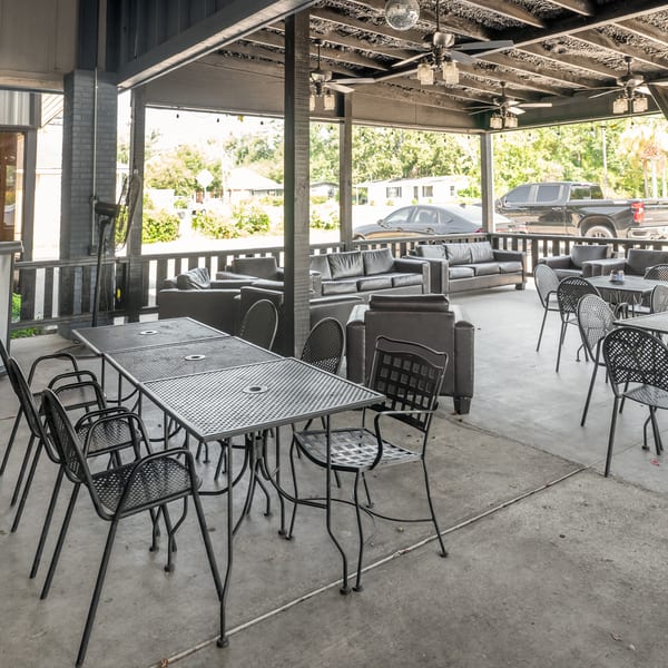 Outdoor patio with black metal tables and chairs, and dark leather sofas under a covered roof.