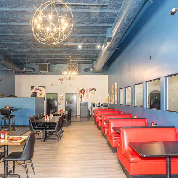Interior of a restaurant with red booths, black tables, and blue walls, featuring modern light fixtures.