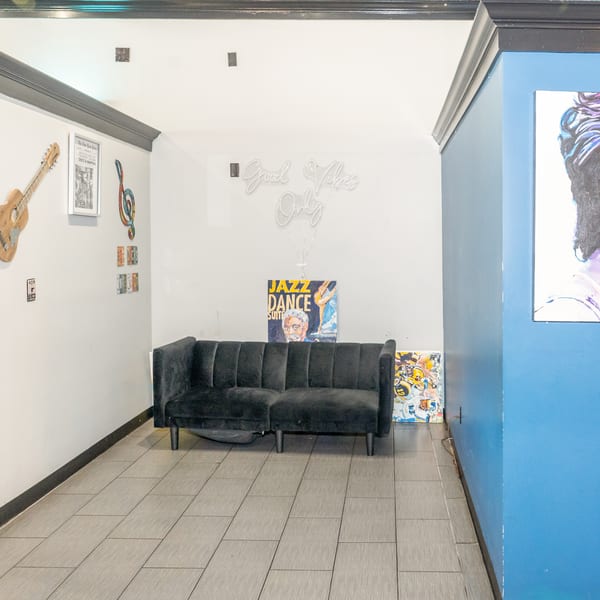 A black velvet sofa sits against a white wall with a "Good Vibes Only" neon sign and art.