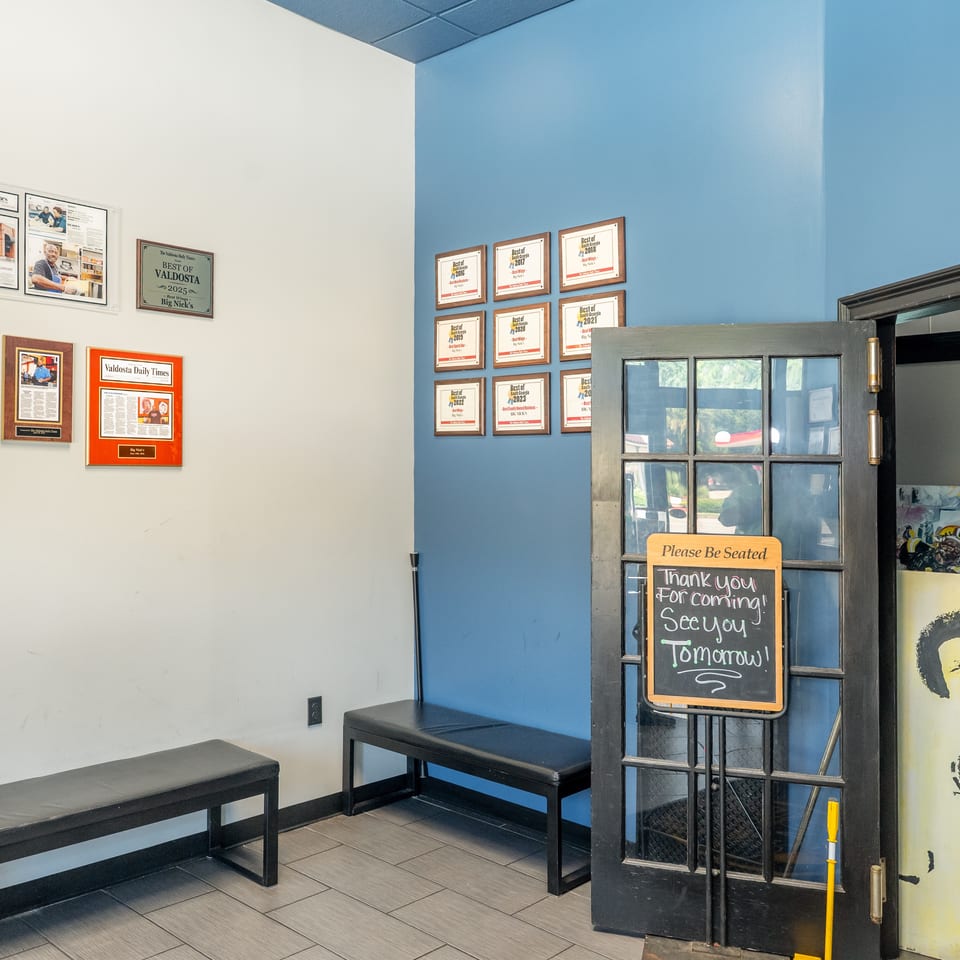 Restaurant entrance with awards on the wall, benches, and a "Please Be Seated" sign on the door.
