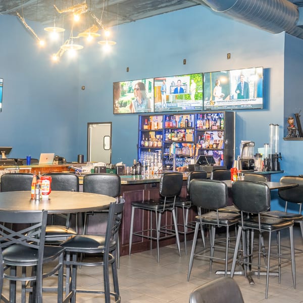 A restaurant interior with blue walls, a bar, high-top tables, and multiple TVs showing sports.