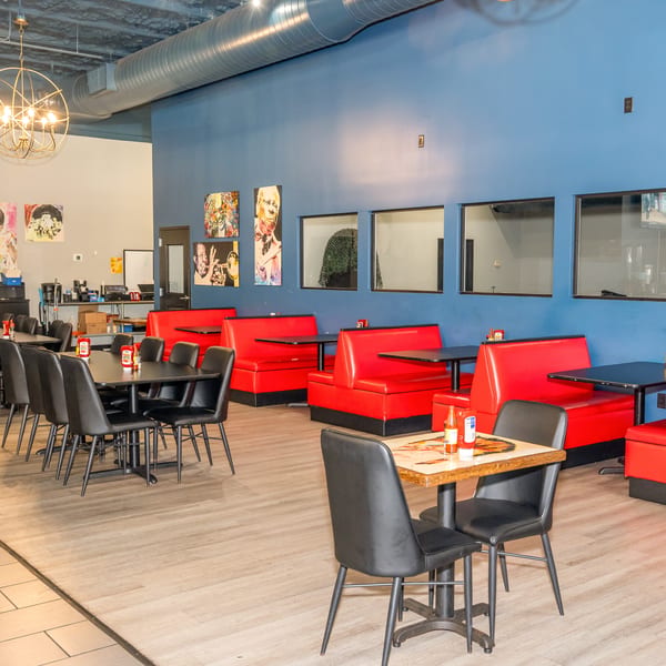 Restaurant interior with red booths, black tables and chairs, blue walls, and modern art.
